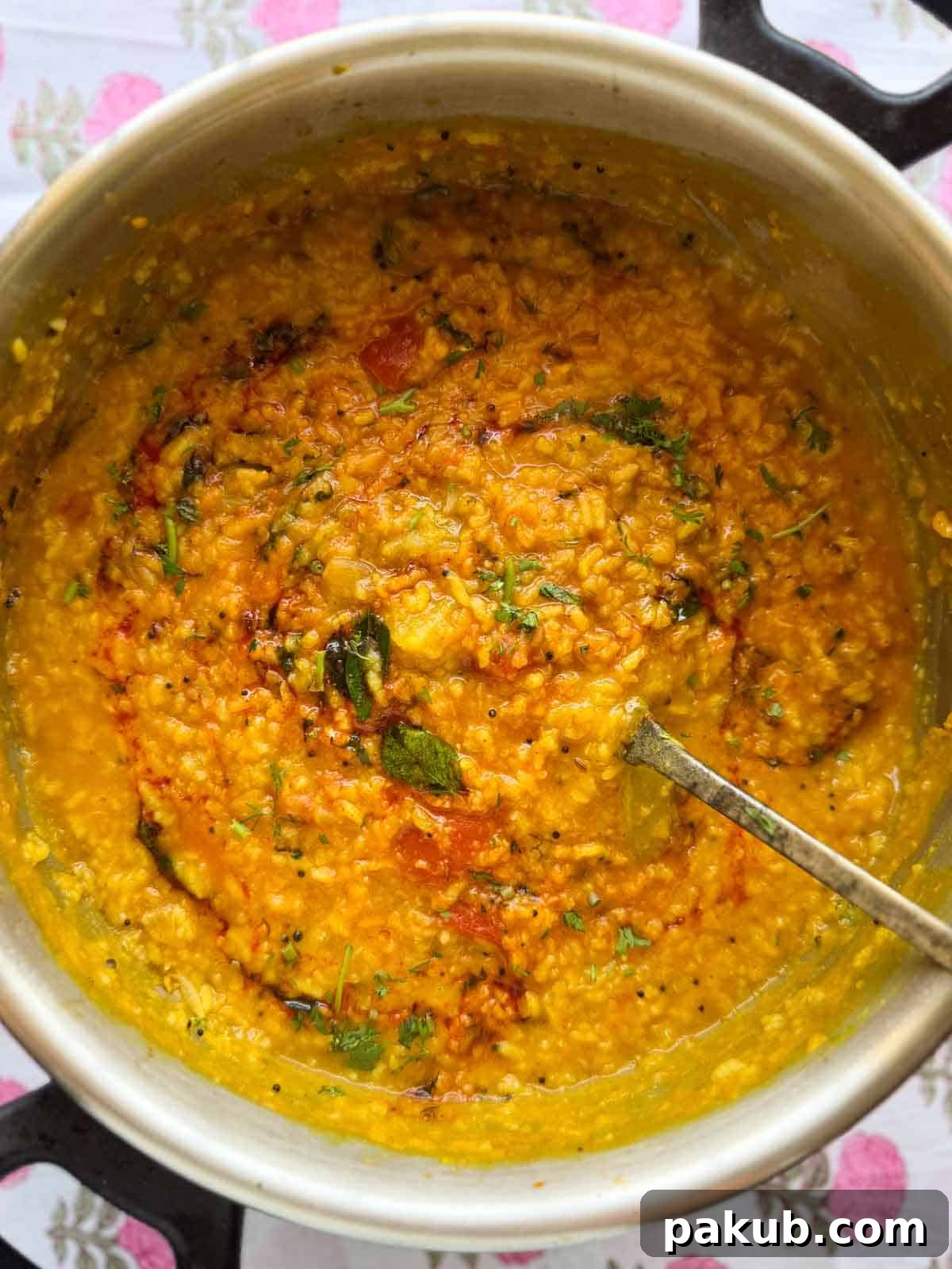 One pot Sambar Rice scooped up in a ladle, showcasing its rich texture and color, garnished with fresh herbs.
