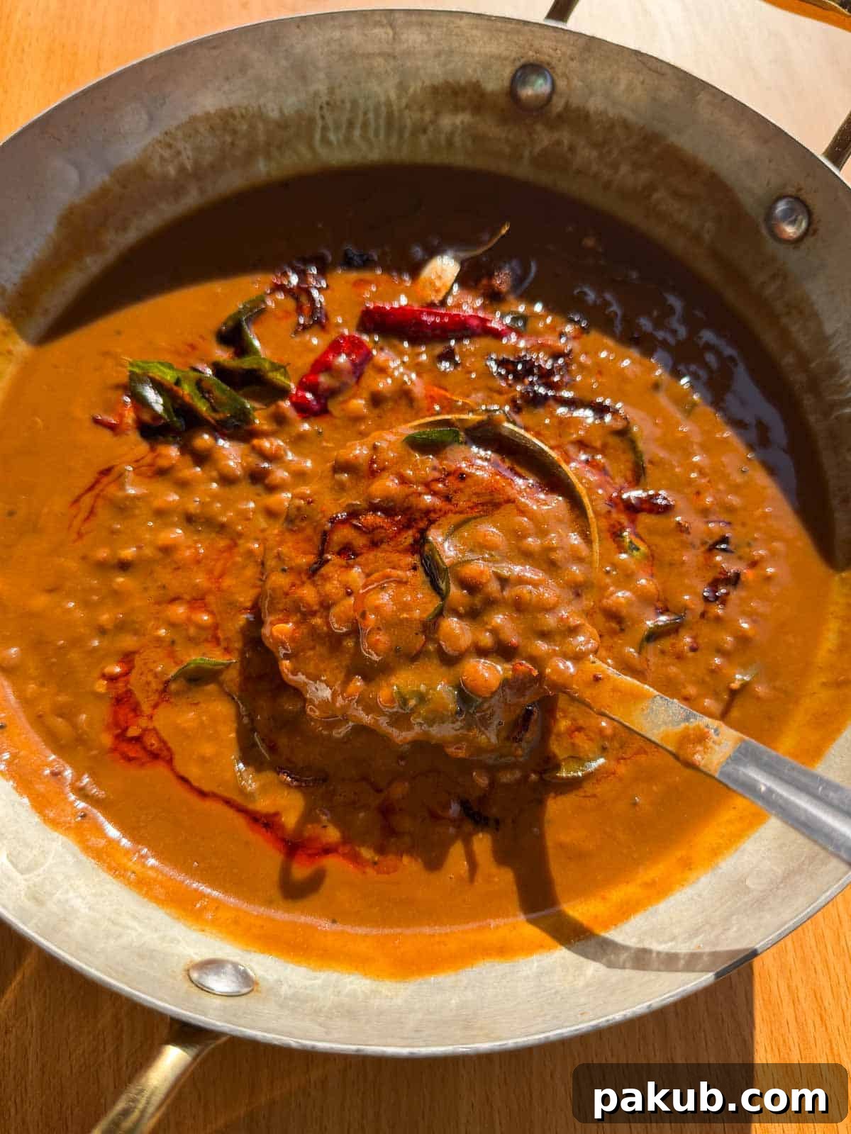 Close-up of freshly made horsegram dal scooped in a ladle, showcasing its rich color and creamy texture, garnished with fresh cilantro.