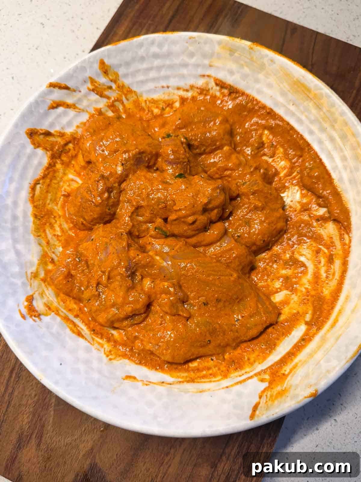 Close-up of bone-in chicken leg pieces marinated in a rich yogurt-spice mixture for Iffa Chicken.