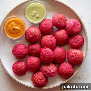 Vibrantly pink Beetroot Paniyaram served on a plate with contrasting coconut chutney and tangy tomato chutney, making for an appetizing display.