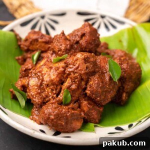 Rich Chicken Ghee Roast served elegantly in a white bowl, resting on a vibrant plantain leaf, a visual feast of flavors.