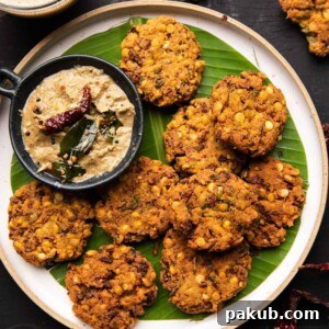 Crispy Masala Vadas served on a banana leaf-lined white plate, accompanied by vibrant coconut chutney on the side, a perfect savory snack.