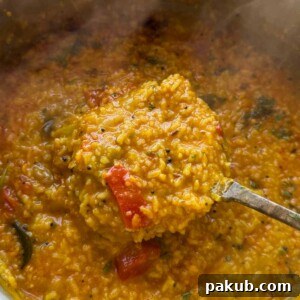 One-pot Sambar Rice, richly flavored, scooped up with a ladle directly from the cooking pot, ready to be served as a comforting meal.