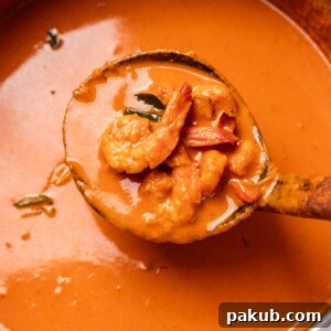 Flavorful Mangalorean Prawn Curry, thick and rich, scooped up in a ladle to showcase its luscious texture and vibrant color.