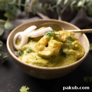 A vibrant bowl of white rice topped with a rich green prawn curry, garnished with roundels of fresh onions, offering a visually appealing meal.
