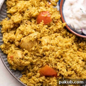 Fragrant Chicken Pulao served on a stylish grey plate, accompanied by cooling raita, making for a delicious and satisfying meal.