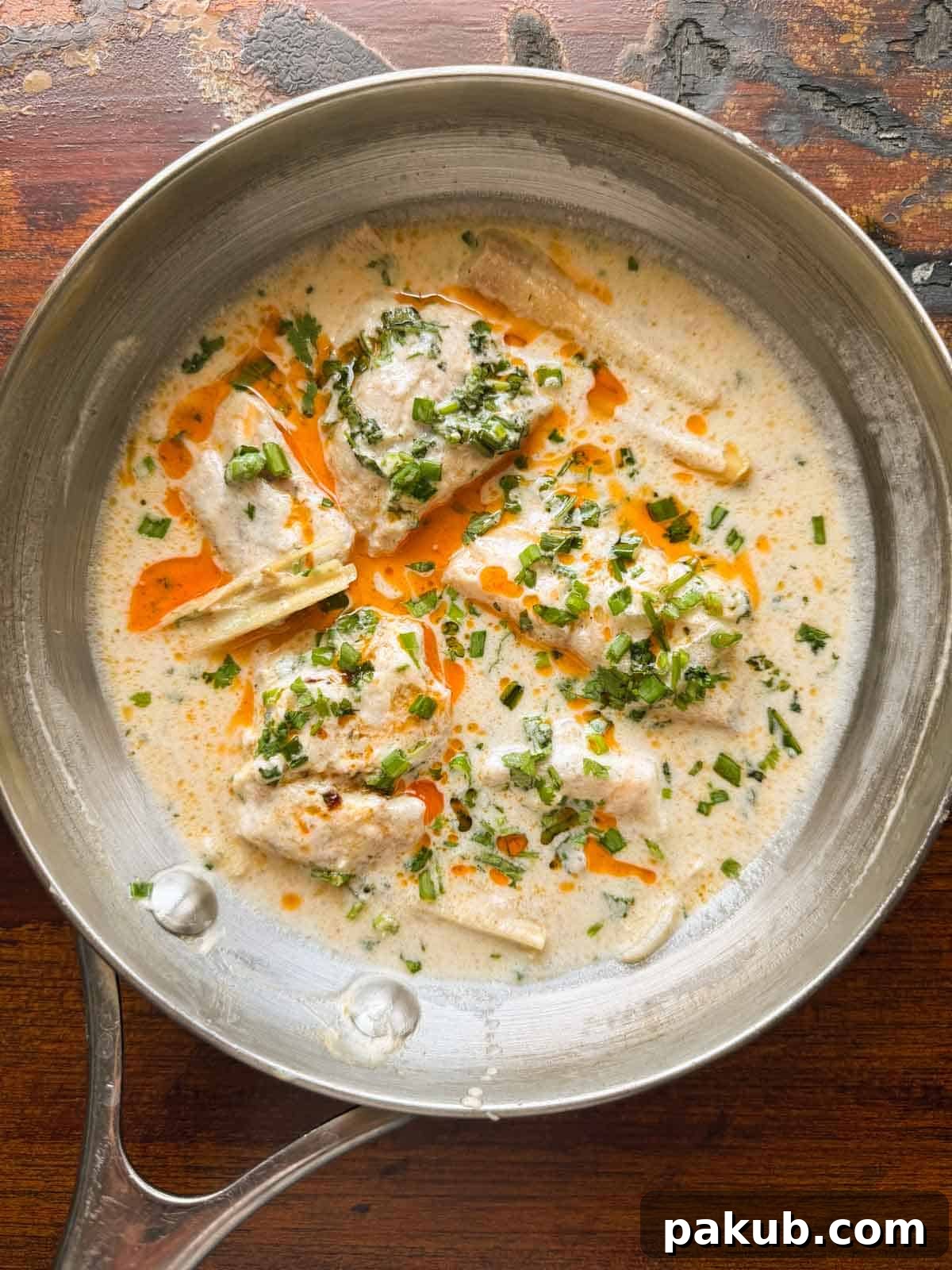 Creamy Thai Coconut Fish 2 A vibrant pan of Thai poached fish in creamy coconut milk, garnished with a sprinkle of fresh chili oil and chopped spring onions, ready to be served.