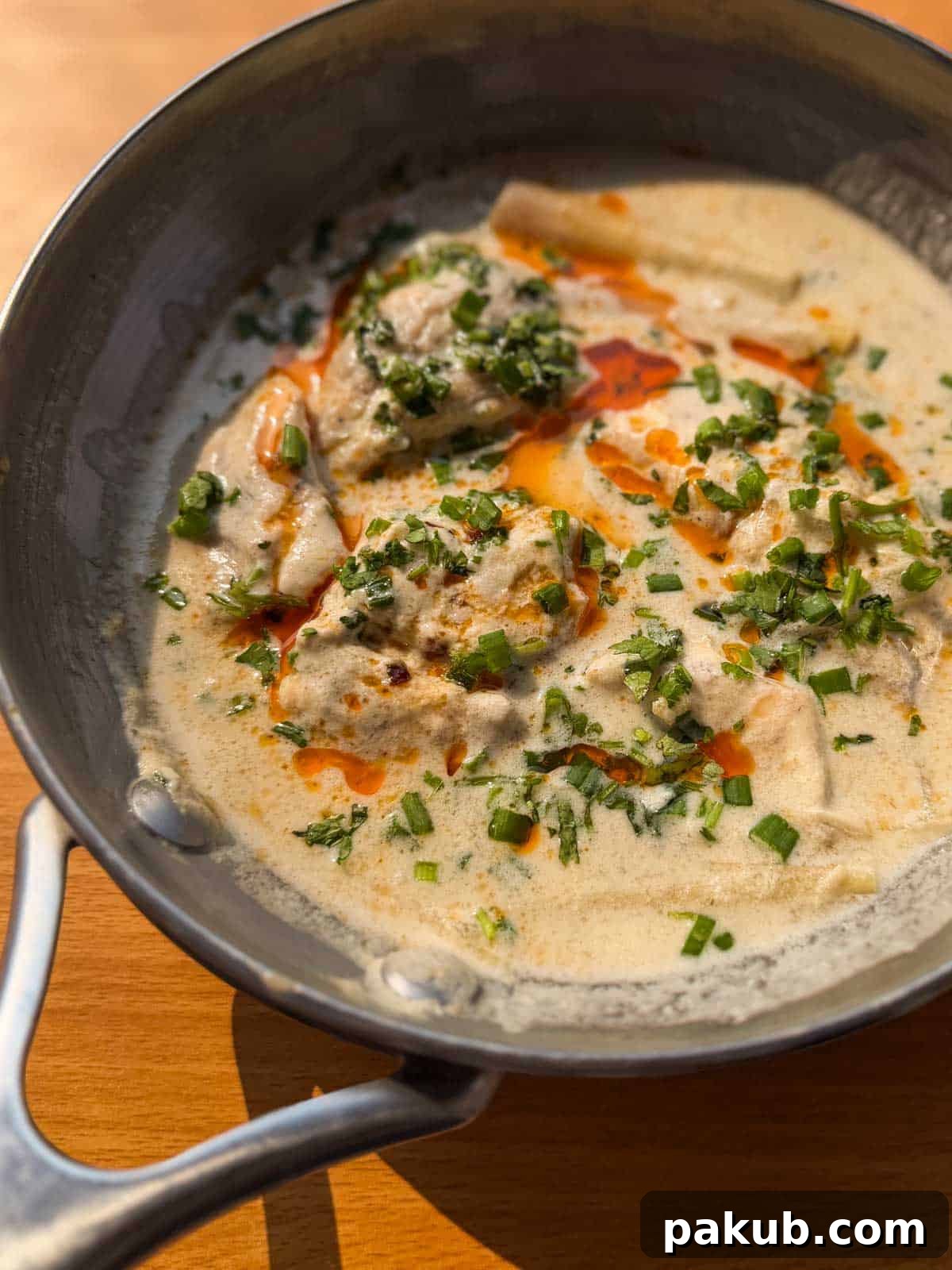 Creamy Thai Coconut Fish 4 A beautifully presented pan of Thai poached fish in coconut milk, generously topped with vibrant chili oil and fresh spring onions, highlighting its readiness to serve.