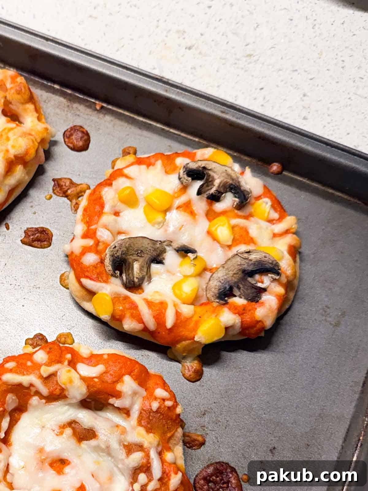 Kid-Friendly Mini Veggie Pizzas 4 Close-up view of a freshly baked mini vegetarian pizza, showing the perfectly melted mozzarella cheese, vibrant corn, and savory mushroom toppings on a golden crust.
