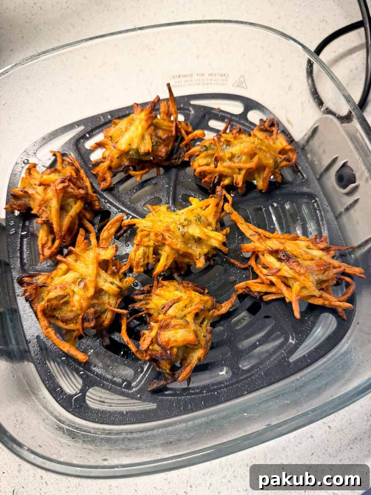 Golden Crispy Air Fryer Veg Pakora 3 A close-up shot of golden, crispy air fryer vegetable pakoras nestled inside an air fryer basket, showing their perfectly cooked texture.