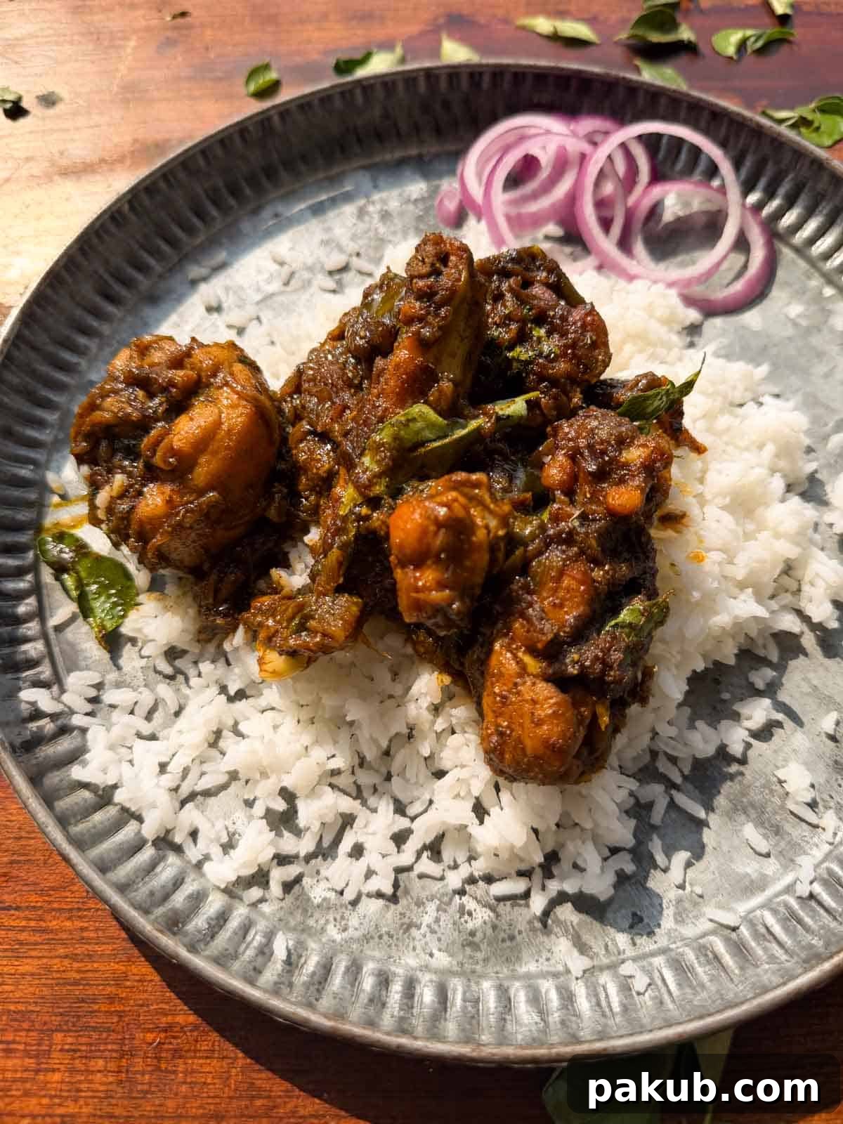 an image of curry leaf chicken served on a bed of rice with sliced onions on the side