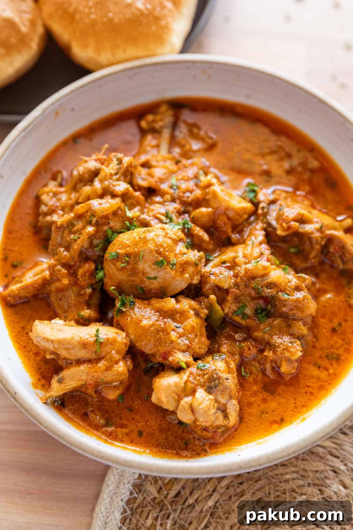 Chatpata dahi chicken in a white bowl with pooris on the side