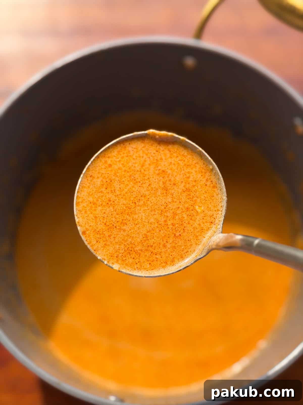 the peanut butter ramen noodle broth scooped up in a ladle to showcase its smooth texture