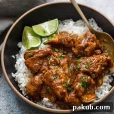 Slow cooker chicken curry served over steamed rice in a black bowl with lemon wedges.