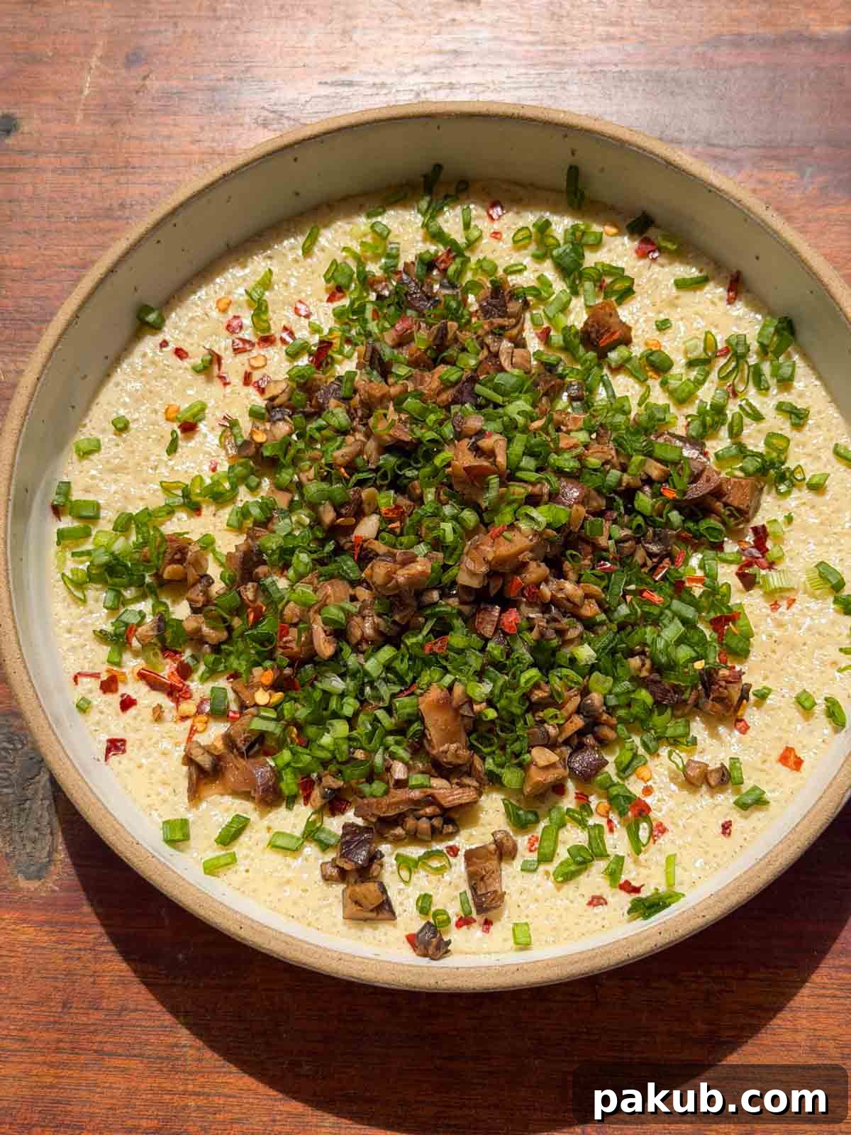 an image of chinese steamed eggs garnished with mushroom and spring onion ready to be eaten