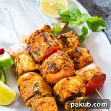 Paneer tikka skewers garnished with mint, lemon and served on a white plate.