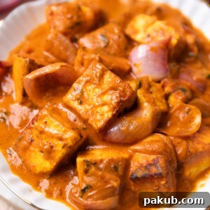 Paneer do pyaza served in a white bowl with accompaniments