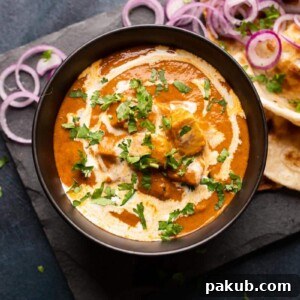 Picture of shahi paneer served in a black bowl with onions and naan on the side