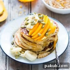 The pancakes topped with seeds, hung curd, sliced mangoes and served on a white plate.