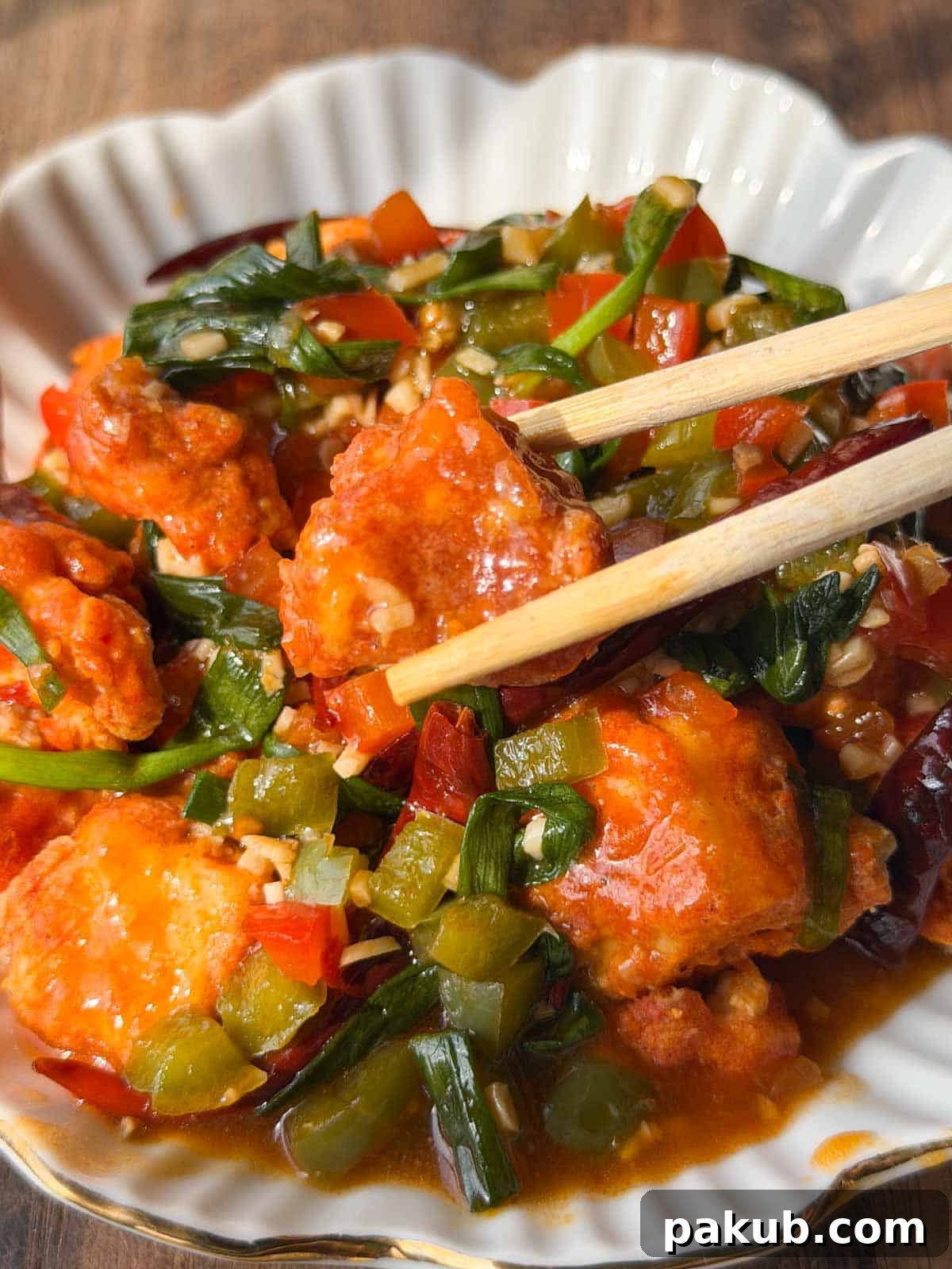 a close up image of crispy chili tofu served in a white bowl with chopsticks
