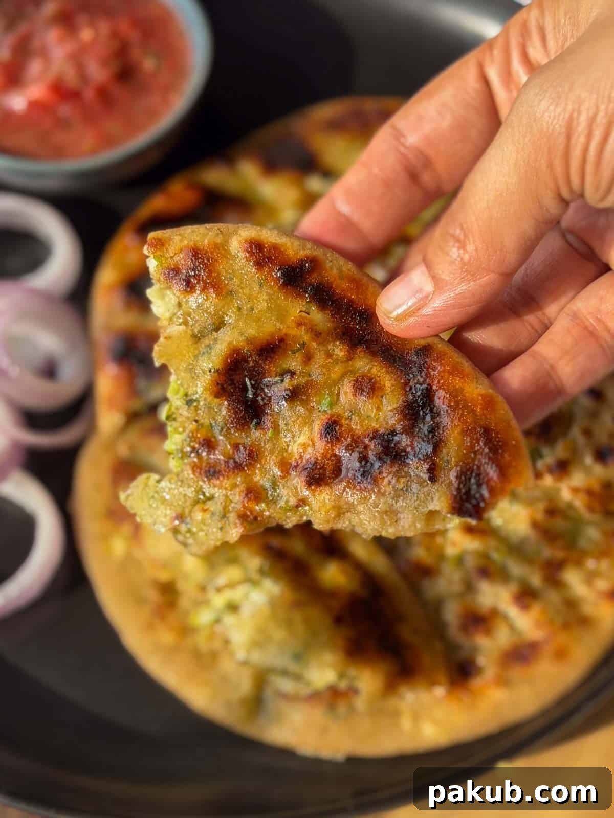 High Protein Stuffed Broccoli Paneer Paratha Recipe 4 a person holding a piece of cook broccoli paneer paratha to showcase it's color and texture
